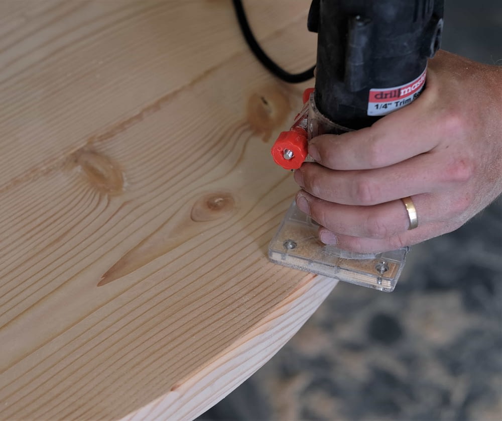 Man using router to round the edges of a rustic coffee table